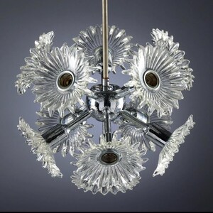 Puede incluir: Un candelabro vintage con pantallas de vidrio transparente en forma de flor. La l&aacute;mpara tiene un cubo central y brazos cromados, con m&uacute;ltiples portal&aacute;mparas. El dise&ntilde;o recuerda la est&eacute;tica moderna de mediados de siglo, ofreciendo una soluci&oacute;n de iluminaci&oacute;n &uacute;nica.