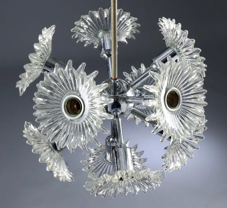 Puede incluir: Un candelabro vintage de estilo moderno de mediados de siglo. La l&aacute;mpara esf&eacute;rica presenta m&uacute;ltiples pantallas en forma de flor de vidrio transparente unidas a un marco de metal cromado. La l&aacute;mpara est&aacute; suspendida de una varilla central.