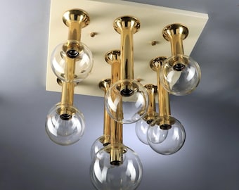 May include: A modern ceiling light fixture featuring a cream-colored square base with eight gold-toned stems. Each stem supports a clear, spherical glass shade, creating a stylish and contemporary lighting design.