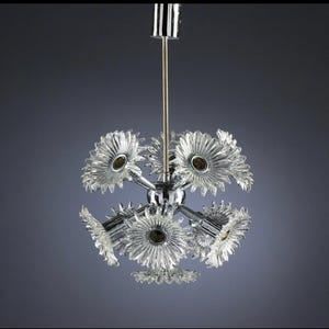 Puede incluir: Una l&aacute;mpara de ara&ntilde;a vintage con acabado cromado y pantallas de vidrio transparente en forma de flor. La l&aacute;mpara tiene m&uacute;ltiples brazos que se extienden desde una esfera central, cada uno con una pantalla en forma de flor. El dise&ntilde;o recuerda la est&eacute;tica moderna de mediados de siglo.