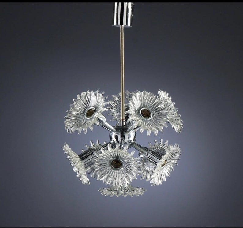 Puede incluir: Una l&aacute;mpara de ara&ntilde;a vintage con acabado cromado y pantallas de vidrio transparente en forma de flor. La l&aacute;mpara tiene m&uacute;ltiples brazos que se extienden desde una esfera central, cada uno con una pantalla en forma de flor. El dise&ntilde;o recuerda la est&eacute;tica moderna de mediados de siglo.
