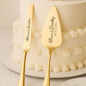 以下が含まれることがあります： 刻印されたテキストが入った、金色のケーキナイフとサーバーのセット。ナイフとサーバーは、装飾的なフロスティングが施された白いケーキの前に表示されています。サーバーには「Allison & Bradley 09.15.2016」と書かれています。