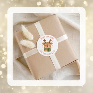 May include: A Christmas gift wrapped in brown paper, tied with a white ribbon, and adorned with dried flowers. A round sticker features a reindeer and the text "Merry Xmas Noah, Love From Mum & Dad."