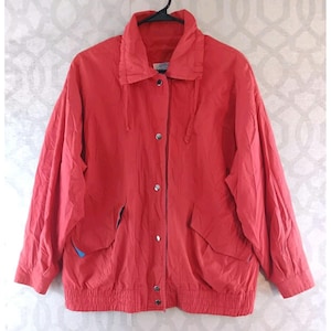 May include: A bright red jacket with a high collar, button closure, and two front pockets. The jacket has a drawstring hood and a ribbed hem and cuffs. The jacket is hanging on a black hanger.