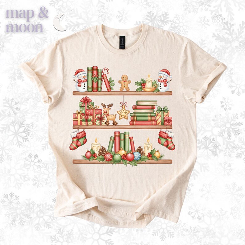 May include: Cream-colored t-shirt featuring a festive bookshelf design. The shelves are adorned with Christmas decorations, including snowmen, books, gifts, candles, and ornaments. The text "map & moon" is in the upper left corner.