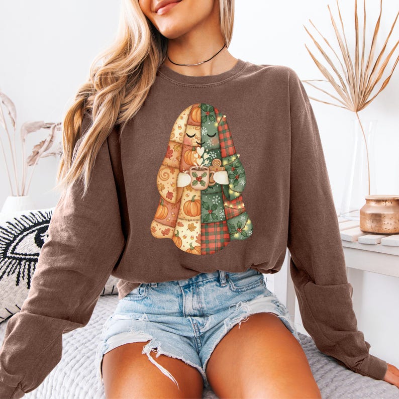 May include: Brown sweatshirt featuring a patchwork ghost design holding a mug. The ghost is composed of autumn-themed patterns, including pumpkins and plaid. The mug has a heart and snowflake design. The sweatshirt is a solid brown color.