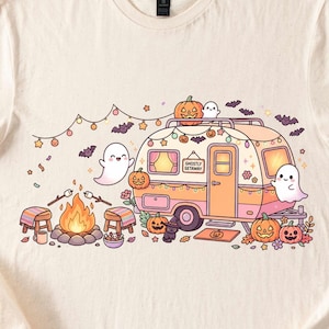 May include: A cream-colored t-shirt featuring a graphic of a vintage camper with the text GHOSTLY GETAWAY. The scene includes ghosts, jack-o'-lanterns, a campfire with marshmallows on sticks, string lights, bats, and a small black cat.