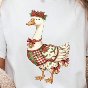 Può includere: T-shirt bianco con un'illustrazione di un'oca ornata da una ghirlanda natalizia, fiocchi rossi e campane. L'oca indossa un gilet festivo con un motivo a quadri rossi e verdi e accenti di agrifoglio. Un design festivo.