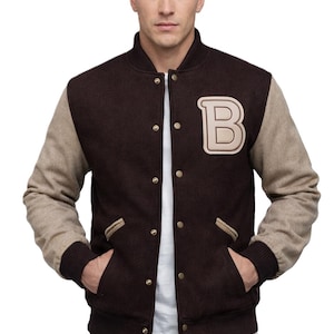 May include: A brown varsity jacket with beige sleeves and a beige letter "B" patch. The jacket has a ribbed collar, cuffs, and hem, and features gold snap closures and pockets. The person is wearing a white shirt underneath.
