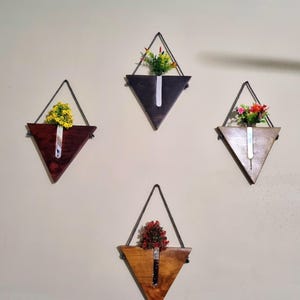 Puede incluir: Cuatro jardineras de pared triangulares de madera con cuerda para colgar. Cada jardinera contiene un pequeño arreglo de flores artificiales de colores. Los tonos de madera varían de marrón oscuro a marrón claro, para la decoración del hogar.