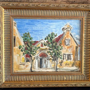 May include: An oil painting in a decorative gold frame depicting a Mediterranean-style building with yellow walls, a red roof, and green trees under a blue sky. The artist's signature, Harris, is visible in the bottom right corner of the canvas.
