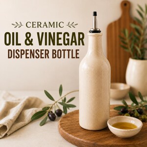 Könnte beinhalten: Eine beige Keramikflasche für Öl und Essig mit einem Ausgießer aus Edelstahl. Der Text CERAMIC OIL & VINEGAR DISPENSER BOTTLE ist in Dunkelgrün und Braun aufgedruckt. Die Flasche hat eine glatte, gesprenkelte Oberfläche und eine zylindrische Form.