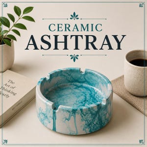 Op de afbeelding: Een ronde keramische asbak met een witte basis, een gemarmerd blauwgroen patroon en vier inkepingen langs de rand. De tekst CERAMIC ASHTRAY staat boven het object, vergezeld door een boek, een kleine plant in een pot en een mok.