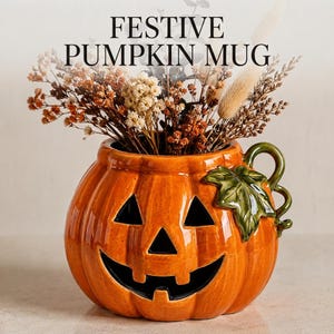 May include: A glossy orange ceramic pumpkin mug featuring a carved jack-o'-lantern face with triangular eyes and a wide grin. A green sculpted leaf and vine handle adorn the side. The mug is filled with dried beige and brown flowers.