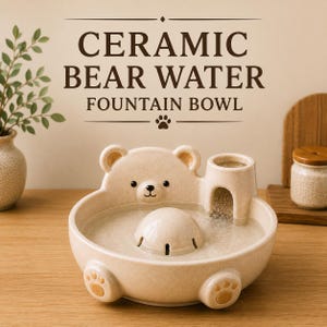 May include: A beige ceramic water fountain bowl shaped like a bear with a central dome and a small tower that dispenses water. The bowl features a bear face, paw prints on the front, and the text CERAMIC BEAR WATER FOUNTAIN BOWL above it.