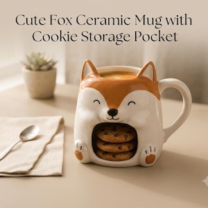 May include: A ceramic mug shaped like a fox with orange and white coloring, featuring a handle on the right side and a hollow compartment at the base for storing cookies. The text "Cute Fox Ceramic Mug with Cookie Storage Pocket" is visible.