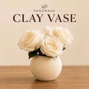 May include: A round, matte off-white clay vase containing a bouquet of white roses with green leaves. The text "HANDMADE CLAY VASE" is printed in dark brown above the flowers, accompanied by a small leaf icon centered above the word handmade.