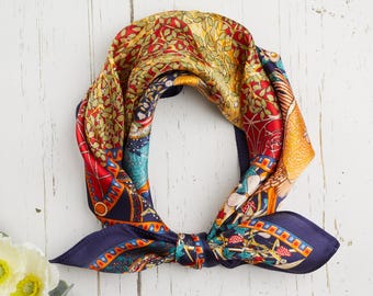 May include: A colorful silk scarf with a detailed pattern. The scarf features a mix of red, yellow, blue, and green hues. The scarf is tied in a knot, showcasing its intricate design and vibrant colors. The scarf is a fashion accessory.