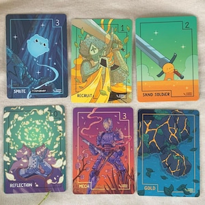 Może przedstawiać: Sześć kart kolekcjonerskich o tematyce fantasy z unikalnymi ilustracjami. Każda karta przedstawia inną postać lub scenę, w tym duszka, rycerza i robota. Karty mają prostokątny kształt z białym obramowaniem i podpisem artysty.