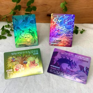 May include: Four rectangular game cards with holographic finishes. Top left: green Tentacle card. Top right: purple Shadow Clone card. Bottom left: green Brush card with cartoon animals. Bottom right: purple Baron Pit card with a dragon illustration.