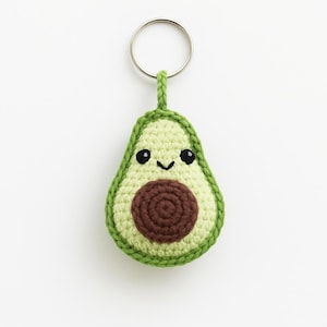 Puede incluir: Llavero de aguacate tejido a ganchillo, con una cara sonriente y una semilla marrón. El aguacate es verde claro con un borde verde oscuro y un llavero plateado. Un accesorio hecho a mano.