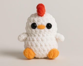 May include: A handmade, white crochet chicken with a red comb, black eyes, and an orange beak and feet. The plush toy is designed in a cute, cartoonish style, perfect for children or as a decorative item.