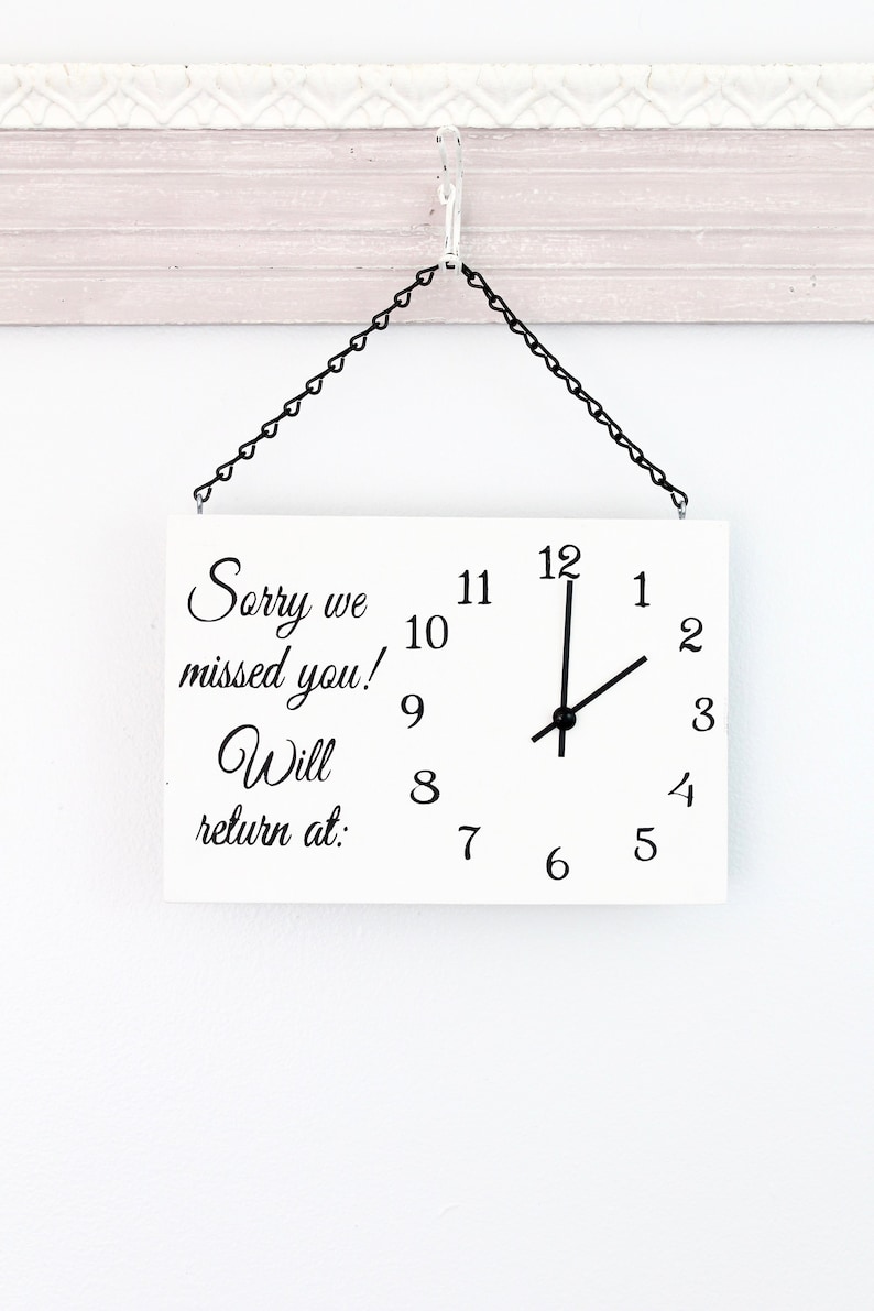 May include: White sign with black text and clock hands. The sign reads "Sorry we missed you! Will return at:". The clock hands are set to 12:30.