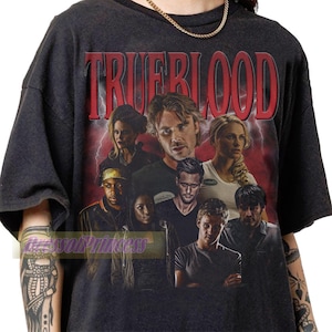 Pode incluir: Uma t-shirt cinzento-carvão de manga curta com uma impressão gráfica do elenco de True Blood. O design inclui o texto vermelho TRUEBLOOD no topo, contra um fundo de relâmpagos vermelhos e uma colagem de personagens da série de televisão.