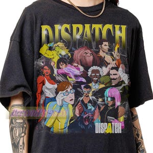 May include: A black short-sleeve t-shirt featuring a large, colourful graphic print of various animated characters. The word DISPATCH is printed in large yellow letters at the top, and the word DISPATCH is also printed in white at the bottom right.
