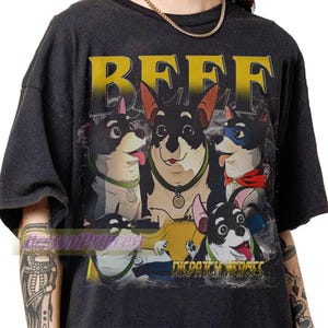 Op de afbeelding: Een antracietgrijs T-shirt met korte mouwen en een grafische print van vijf zwart-witte honden. De tekst BEEF staat in grote gele letters bovenaan en de tekst DISPATCH HEROES is in het geel onderaan de afbeelding gedrukt.