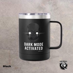 May include: Black travel mug with a silver rim and handle. The mug features a white skull graphic with glowing eyes and the text "DARK MODE ACTIVATED". The mug has a black handle and a silver lid.