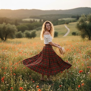 May include: A woman wearing a white off-the-shoulder top and a red plaid skirt twirls in a field of wildflowers. She holds a straw hat, with a scenic background of rolling hills and a winding road.