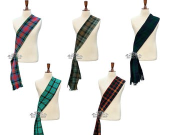 Op de afbeelding: Vijf tartan sjerpen in verschillende kleuren en patronen, gedrapeerd over mannequin torso's. De sjerpen hebben verschillende ruitpatronen, waaronder rood, groen, blauw en geel. De tekst "Available in 50+ Tartans" staat bovenaan.