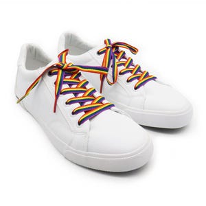 Könnte beinhalten: Ein Paar weiße Sneaker mit regenbogenfarbenen Schnürsenkeln. Die Schnürsenkel zeigen ein lebendiges Farbspektrum, darunter Rot, Orange, Gelb, Grün, Blau und Lila. Die Schuhe haben ein klassisches Low-Top-Design.