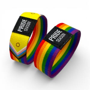 Può includere: Due braccialetti in tessuto. Uno è giallo con un design a strisce multicolore e un'etichetta nera con la scritta "PRIDE SEASON". L'altro braccialetto è un arcobaleno di colori con un'etichetta nera con la scritta "PRIDE SEASON".