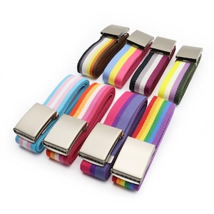 Pode incluir: Uma coleção de cintos de lona coloridos com fivelas de metal prateado. Os cintos apresentam vários padrões listrados em tons de azul, rosa, vermelho, roxo, verde e arco-íris. Os cintos são exibidos em um fundo branco.