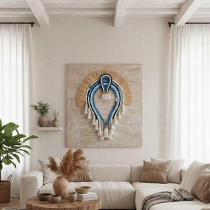 May include: A light and airy living room with a cream-colored sofa, a wooden coffee table, and a decorative wall hanging with blue and beige details. The room is complemented by white curtains and a large potted plant, creating a relaxed and inviting space.