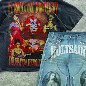 May include: A black graphic t-shirt and denim shorts set. The t-shirt features a colorful graphic with text in Spanish. The denim shorts have the word "HOLYSAINT" and two oval portraits.