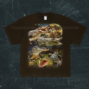 May include: Brown t-shirt featuring a detailed graphic of several alligators with open mouths, set against a backdrop of a full moon and starry sky. The design showcases the alligators in various poses, highlighting their textures and colors.