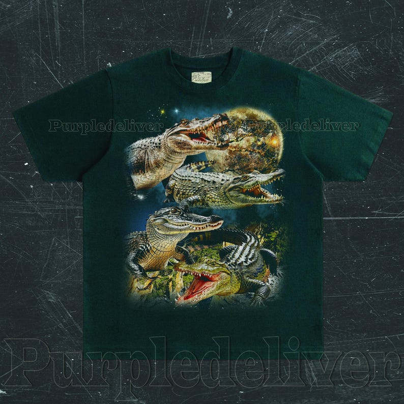 May include: Dark green t-shirt featuring a detailed graphic of several alligators with open mouths, set against a night sky and a full moon. The design includes various shades of green, brown, and white, creating a striking contrast on the shirt.