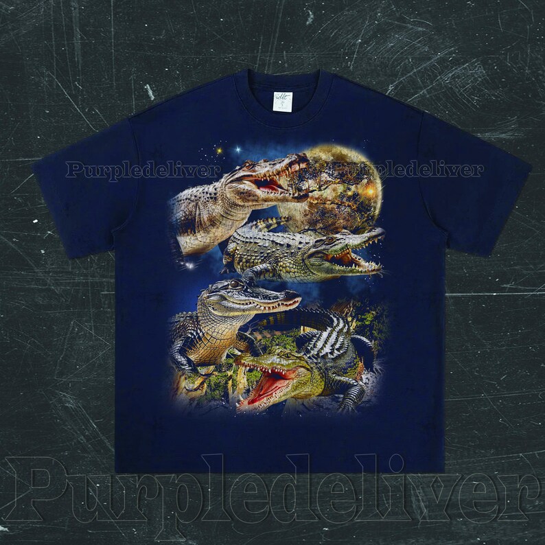 May include: Navy blue t-shirt featuring a graphic of several alligators with open mouths, set against a backdrop of a full moon and starry sky. The design includes detailed illustrations of the reptiles.