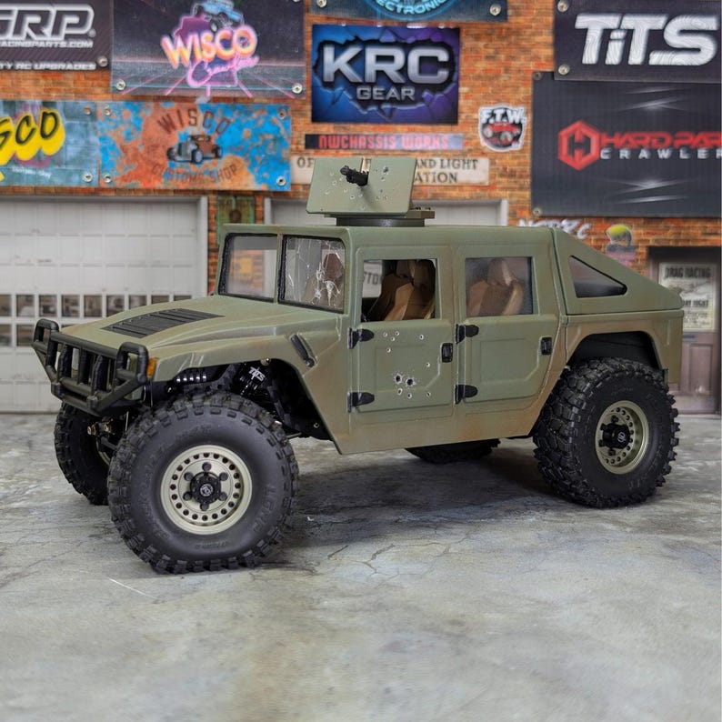 Puede incluir: Un modelo Humvee verde oliva con una ametralladora montada. El veh&iacute;culo de juguete tiene neum&aacute;ticos grandes y resistentes y detalles, incluidos agujeros de bala simulados. El fondo presenta se&ntilde;alizaci&oacute;n de estilo garaje.