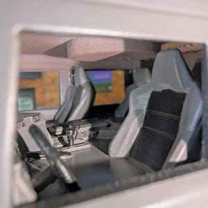 Puede incluir: Interior detallado de un modelo de veh&iacute;culo, con asientos grises y negros, volante y salpicadero. La imagen ofrece una vista del &aacute;rea del conductor, con controles visibles y un vistazo del exterior a trav&eacute;s de las ventanas.