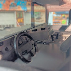 Puede incluir: Vista interior del salpicadero de un veh&iacute;culo, con volante, palanca de cambios y rejillas de ventilaci&oacute;n. El salpicadero es de color gris oscuro, con un acabado brillante. El parabrisas es visible, con un fondo borroso.