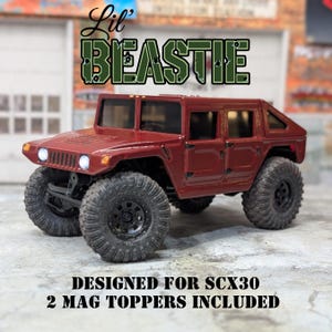 May include: A maroon-colored toy Hummer with large black tires. The text "Lil' BEASTIE" is above the vehicle, and the text "DESIGNED FOR SCX30 2 MAG TOPPERS INCLUDED" is below. The toy has a detailed design.