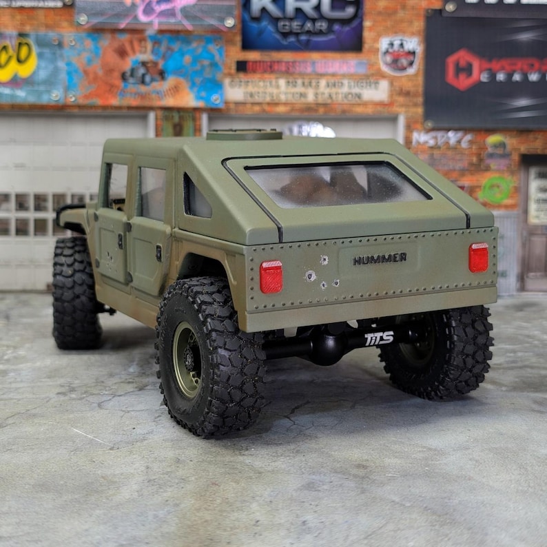 Puede incluir: Modelo Hummer verde oliva con neum&aacute;ticos grandes y robustos. La parte trasera del veh&iacute;culo muestra la palabra "HUMMER" y las letras "TTS". El modelo tiene una ventana trasera transparente y orificios de bala simulados.