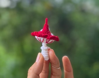 May include: A small crocheted mushroom with a red cap and white stem.