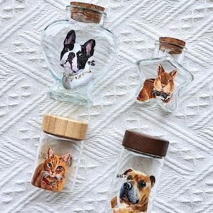 Op de afbeelding: Vier doorzichtige glazen potten met kurken of houten deksels, elk voorzien van een handgeschilderd dierenportret. De collectie bevat een hartvormige pot met een buldog, een stervormige pot met een konijn en twee cilindervormige potten met een kat en een hond.