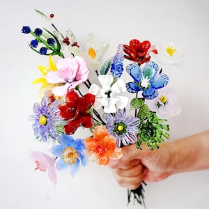 May include: A colorful bouquet of glass flowers in various shapes and sizes. The flowers are in shades of red, blue, pink, orange, and white, with green stems and leaves. The bouquet is held together at the base.
