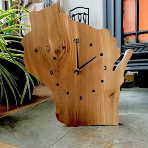 May include: A wooden clock shaped like the state of Wisconsin. The clock face has black hands and black numbers.